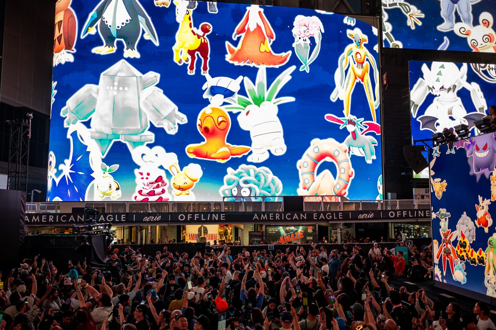 时代广场上数千名 Pokémon Go 玩家聚集，手机屏幕和广场大屏同步展示超梦团战画面
