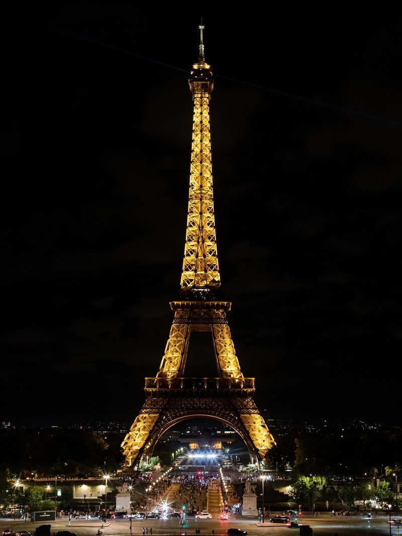 La luz ámbar cálida de la Torre Eiffel, proyectada por 336 proyectores de sodio de alta presión, contrasta fuertemente con la luz blanca y cegadora de los puestos callejeros