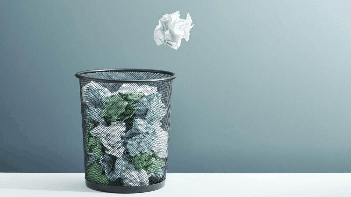 A crumpled ball of paper flies toward a overflowing trash can